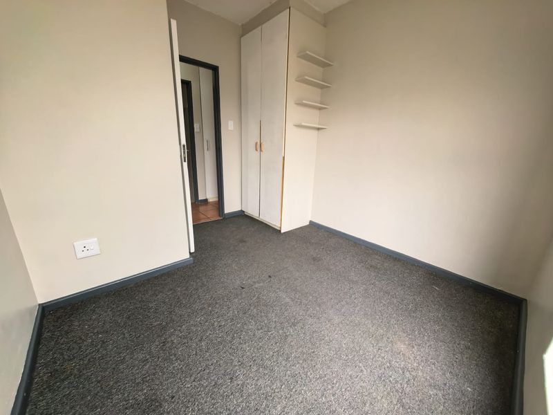An empty bedroom featuring built-in wardrobe storage, fitted wall shelving, and carpeted flooring, ready for personalization.