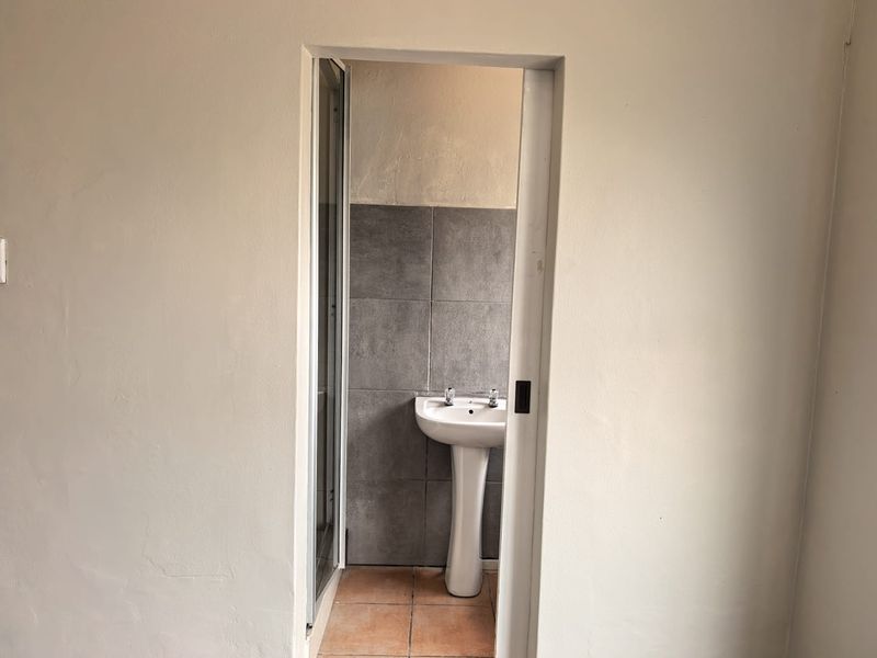 A compact bathroom featuring a pedestal basin, tiled splashback, and a shower enclosure, accessed via a sliding door.
