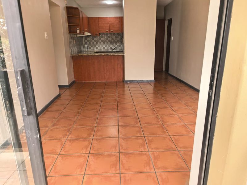 An open-plan living and kitchen area featuring terracotta-style floor tiles, built-in wooden cabinetry, granite countertops, and direct access to an outdoor space.