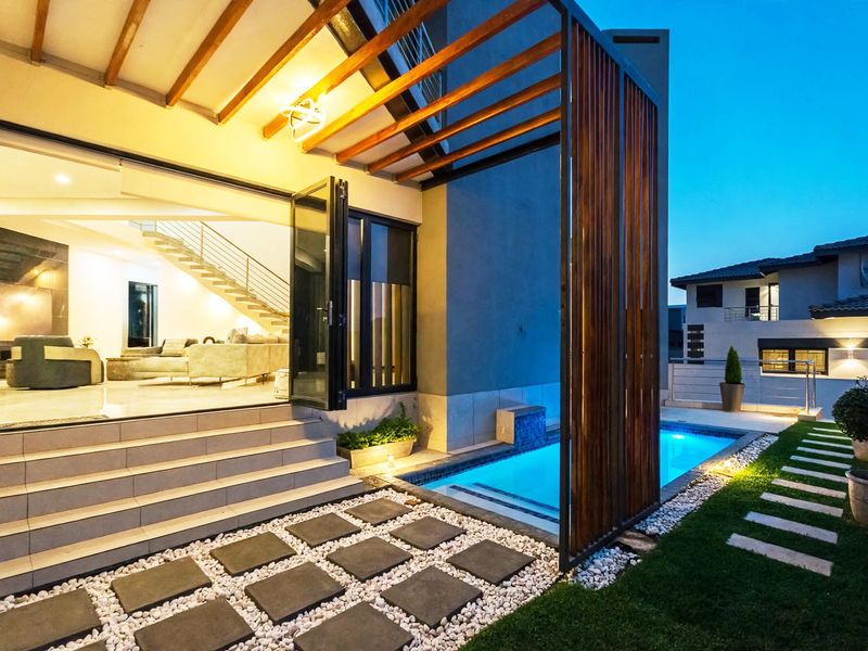 Modern outdoor pool area featuring a timber pergola, stone pavers, and seamless indoor-outdoor flow through large bi-fold doors into the living space.