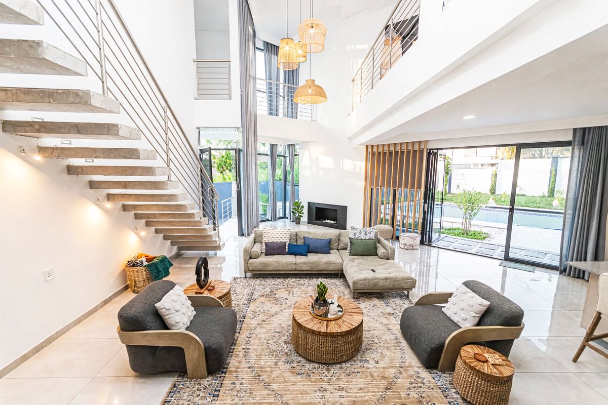 Spacious double-volume living room featuring a modern floating staircase, built-in fireplace, and large sliding glass doors opening to the outdoor pool area.