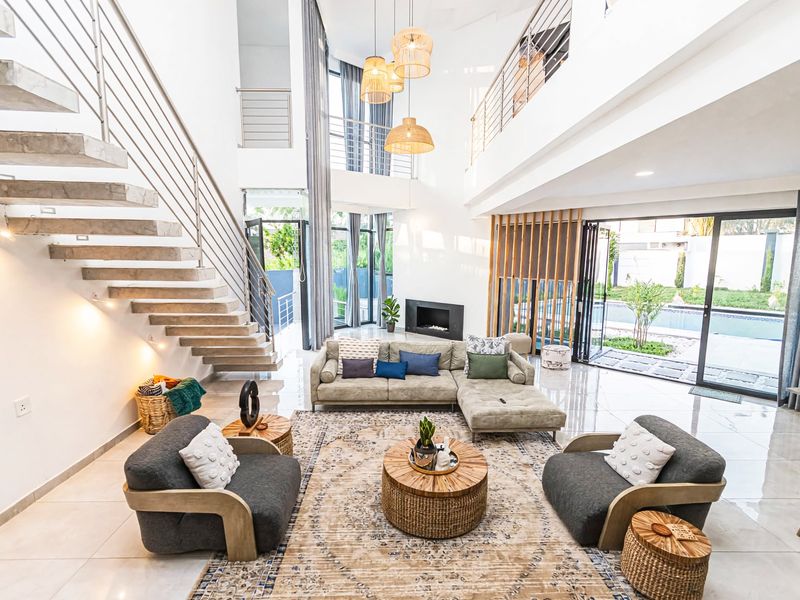 Spacious double-volume living room featuring a modern floating staircase, built-in fireplace, and large sliding glass doors opening to the outdoor pool area.