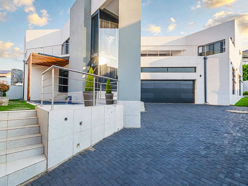 Modern architectural home featuring a paved driveway, double garage, stainless steel balustrades, and a timber pergola over a raised patio area.