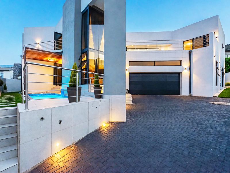 Modern architectural home featuring a paved driveway, double garage, integrated swimming pool, and upper-level balcony with stainless steel balustrades.