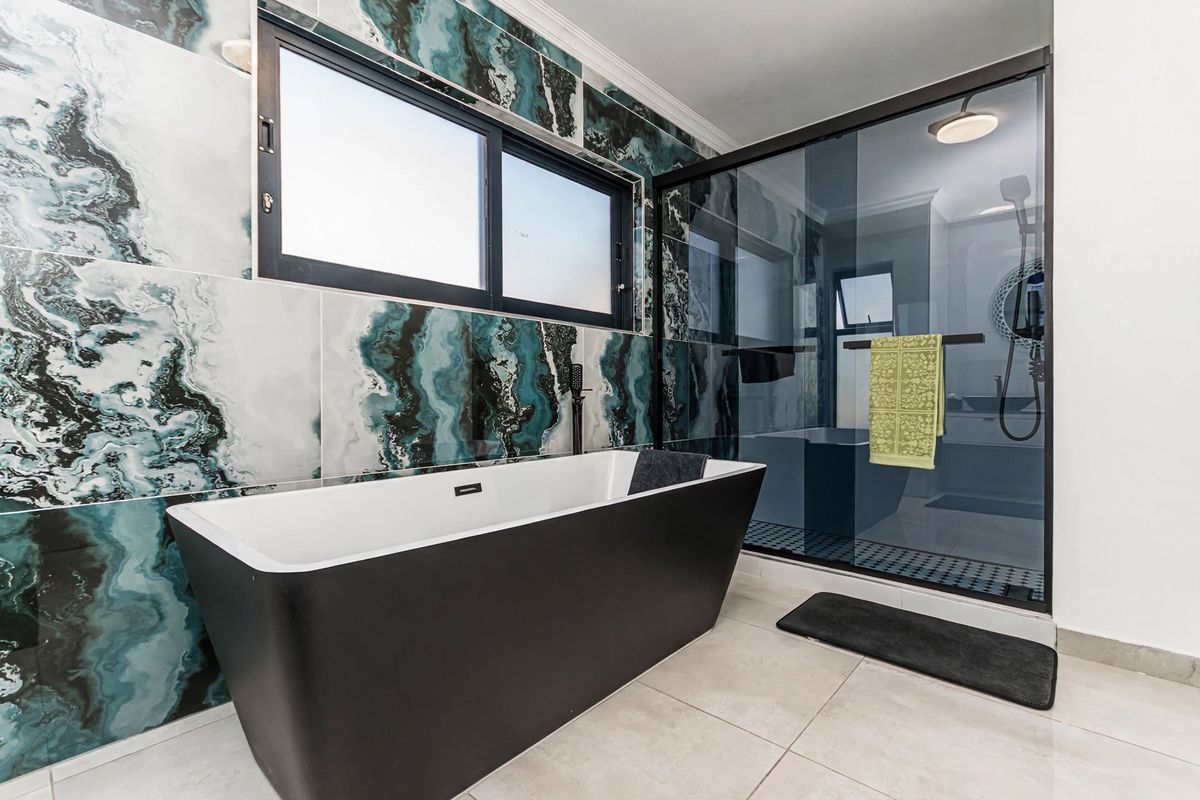 Modern bathroom featuring a sleek black freestanding bathtub, a spacious walk-in shower with glass enclosure, and striking marble-effect wall tiling.