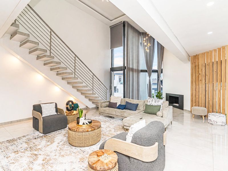 Spacious double-volume living room featuring a modern floating staircase, built-in fireplace, large floor-to-ceiling windows, and elegant timber slat wall detailing.