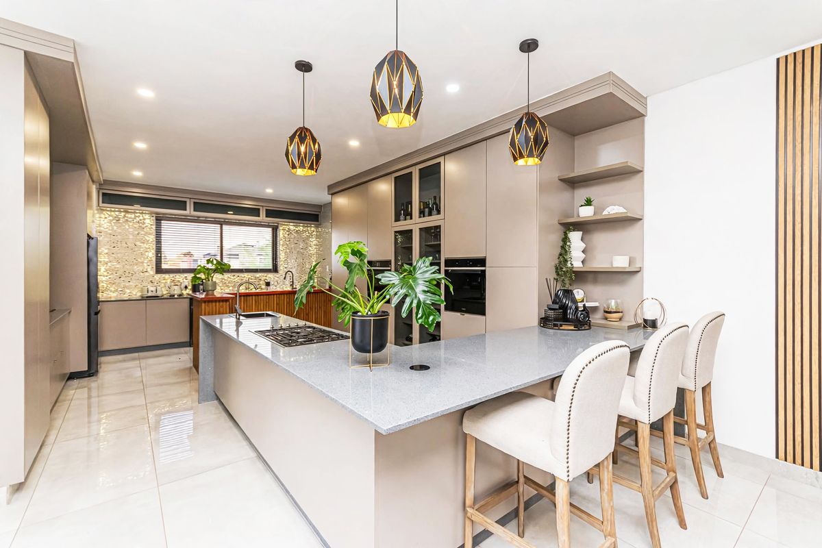 Modern kitchen featuring a large island with stone countertops, built-in appliances, mosaic tile backsplash, and elegant pendant lighting.