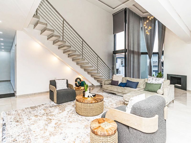 Spacious double-volume living room featuring a modern floating staircase, large windows with floor-to-ceiling curtains, and a sleek built-in fireplace.