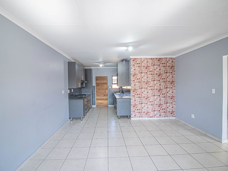 A functional kitchen area featuring grey built-in cabinetry, a gas hob, extractor fan, and a decorative brick-effect feature wall with neutral tiled flooring.