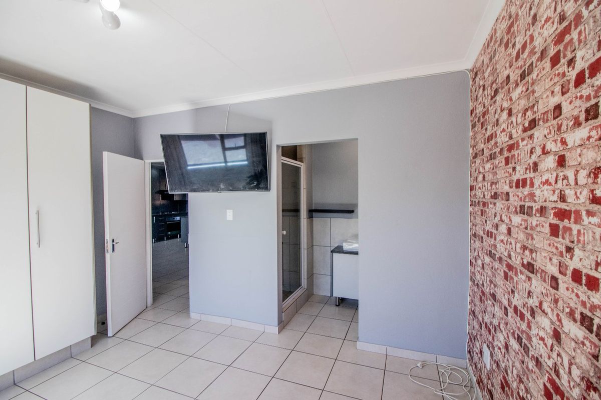 A bedroom featuring tiled flooring, a built-in wardrobe, and an exposed brick feature wall, with direct access to an en-suite bathroom.