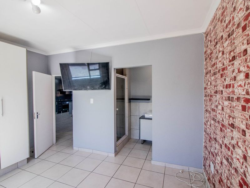 A bedroom featuring tiled flooring, a built-in wardrobe, and an exposed brick feature wall, with direct access to an en-suite bathroom.