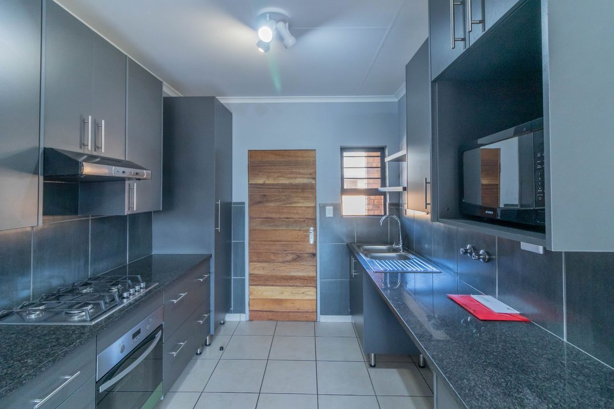 Modern kitchen featuring dark grey cabinetry, granite countertops, gas hob, electric oven, and tiled flooring in a clean, functional layout.