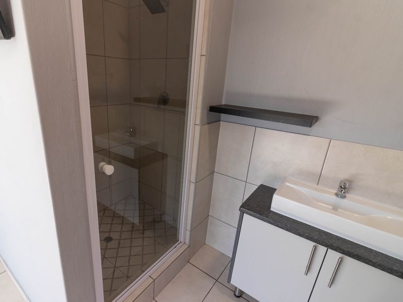 A clean, modern bathroom featuring a glass-enclosed shower, a vanity cabinet with a basin, and neutral wall and floor tiling.