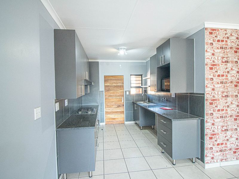 Modern kitchen featuring dark grey cabinetry, granite countertops, a gas hob, and a stylish brick feature wall with tiled flooring.