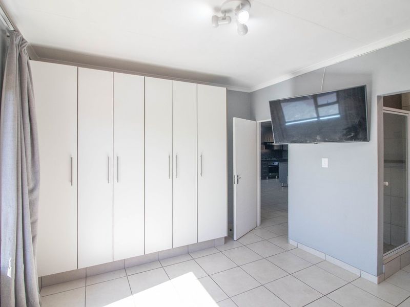 A well-maintained bedroom featuring built-in cupboards, tiled flooring, and an en-suite shower area.