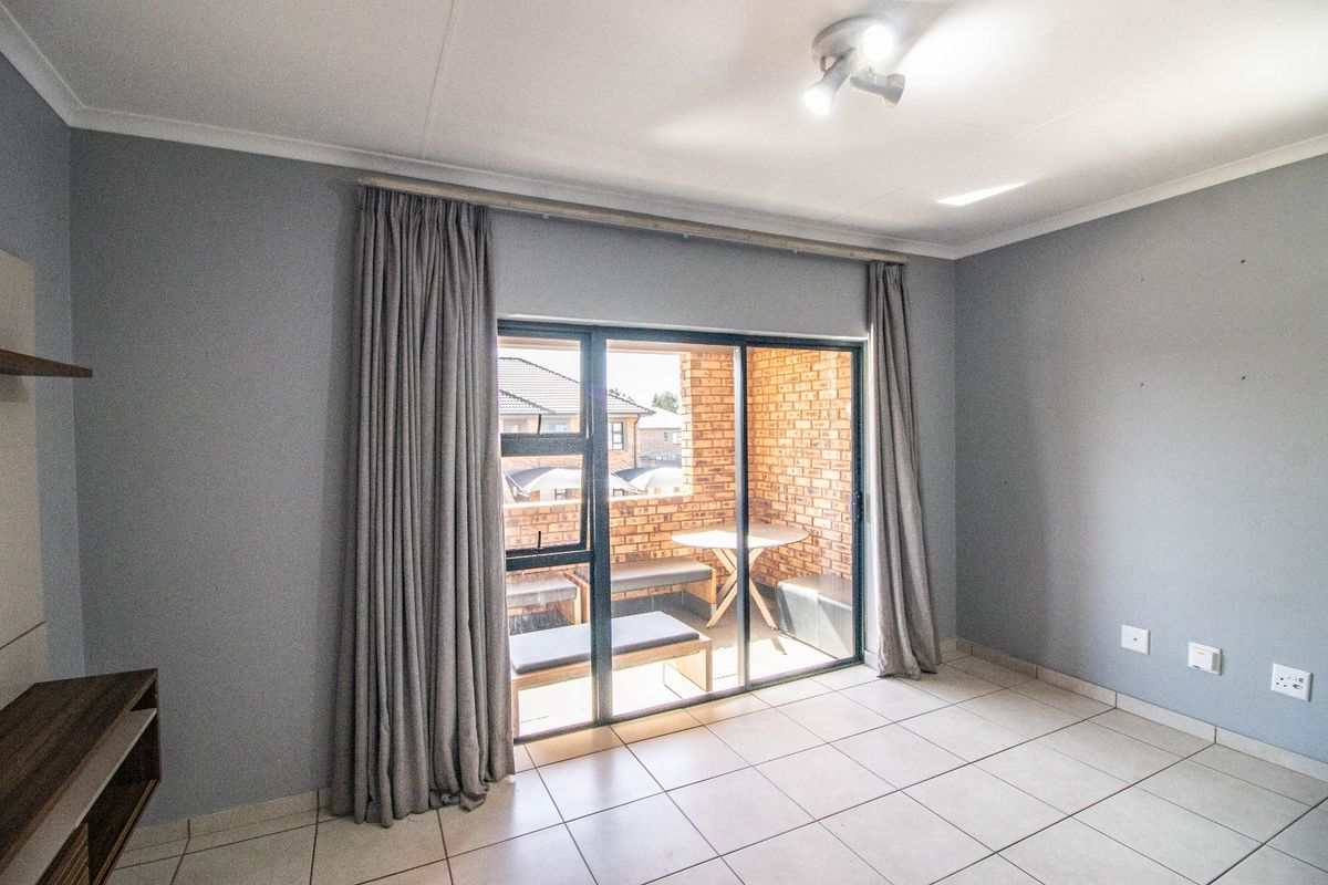 A bright, empty living room featuring tiled flooring and a large sliding glass door that opens onto a private brick-walled balcony.