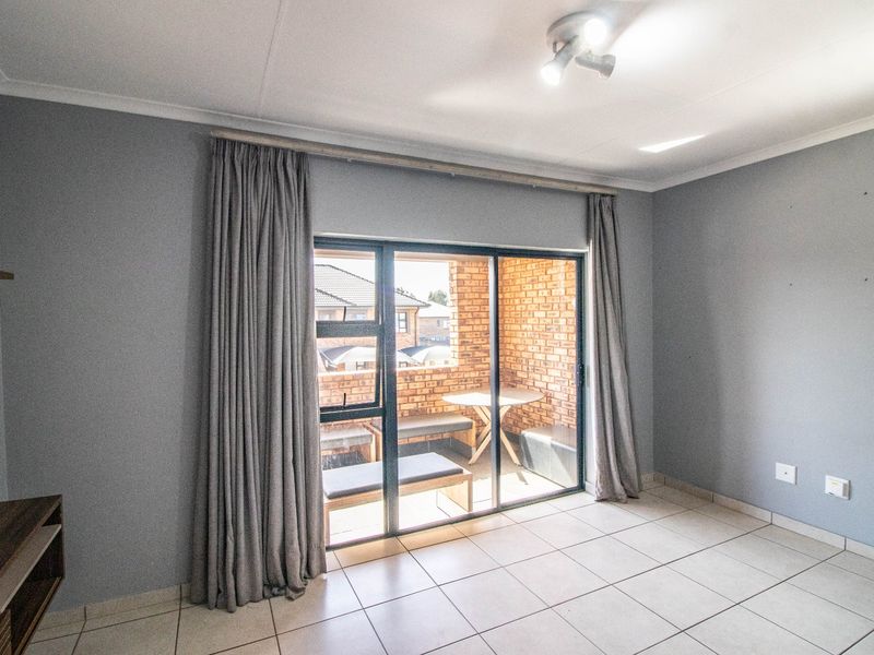 A bright, empty living room featuring tiled flooring and a large sliding glass door that opens onto a private brick-walled balcony.