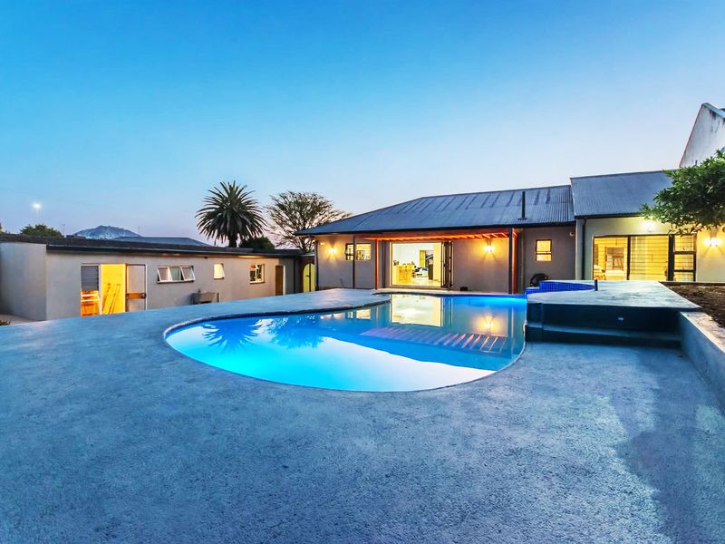 A well-maintained outdoor pool area featuring a concrete deck, covered patio space, and exterior lighting, perfect for evening relaxation and entertainment.