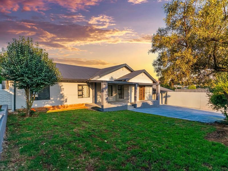 Rear view of the house featuring a covered patio, concrete driveway, and a well-maintained lawn area enclosed by a perimeter wall.