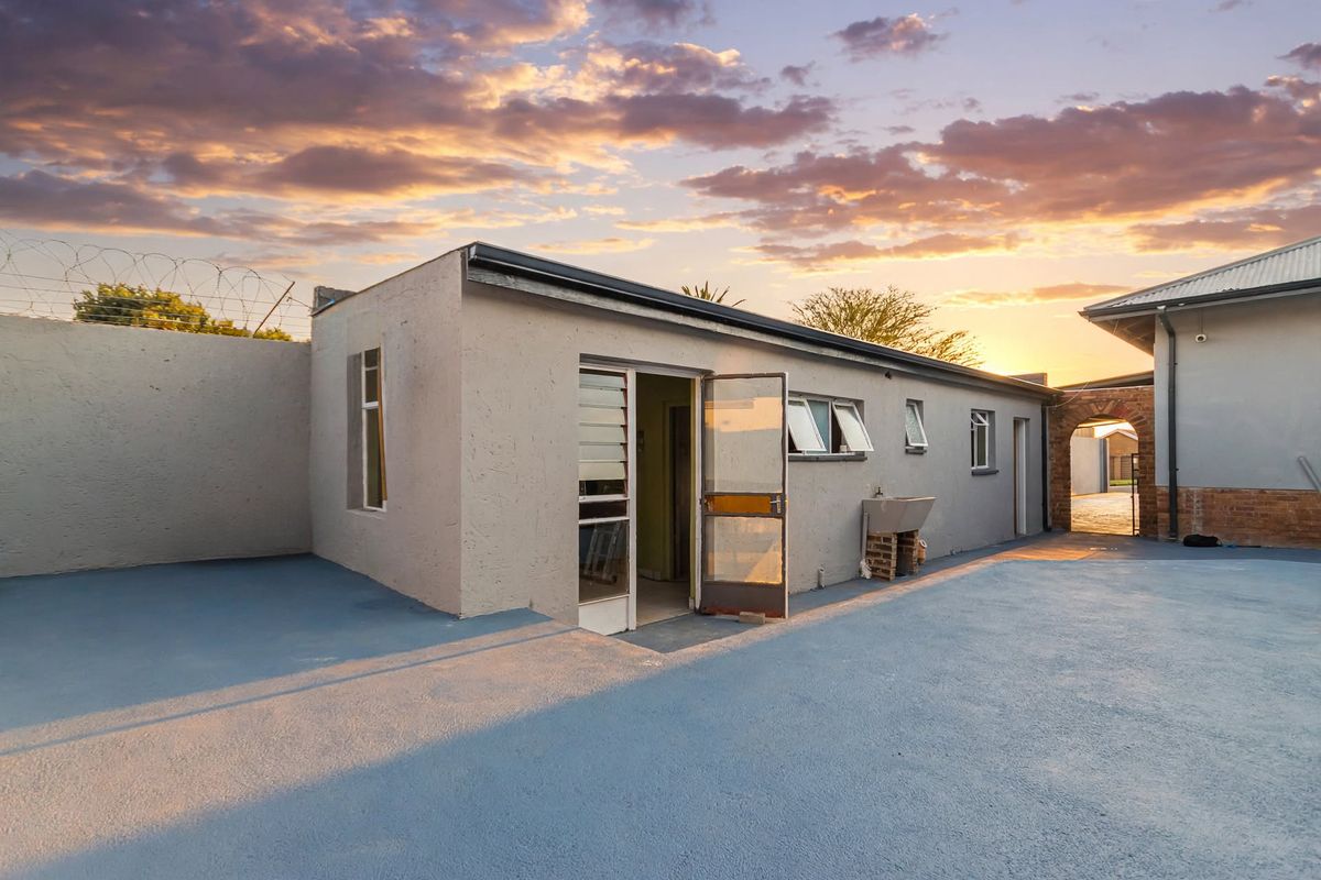 Rear exterior view of the property featuring a paved courtyard, external utility sink, and secure perimeter walling with razor wire.