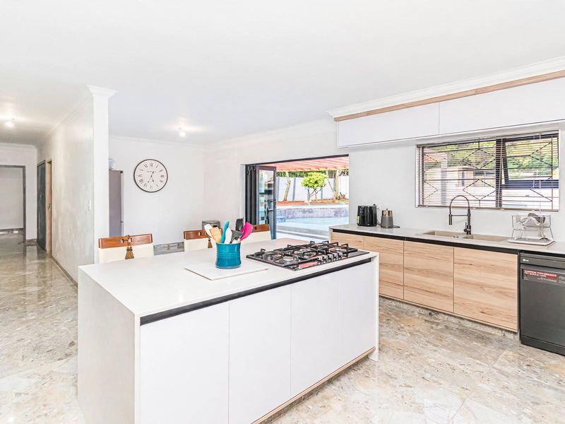 Modern kitchen featuring a central island with gas hob, light wood cabinetry, stone countertops, and seamless access to the outdoor patio area.