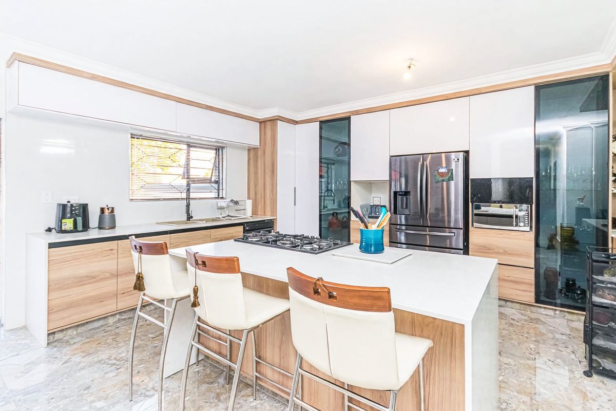 Modern kitchen featuring a central island with a gas cooktop, sleek wood-tone and white cabinetry, stone countertops, and high-quality tiled flooring.