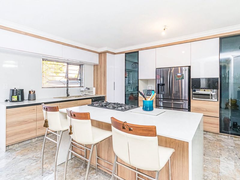 Modern kitchen featuring a central island with a gas cooktop, sleek wood-tone and white cabinetry, stone countertops, and high-quality tiled flooring.
