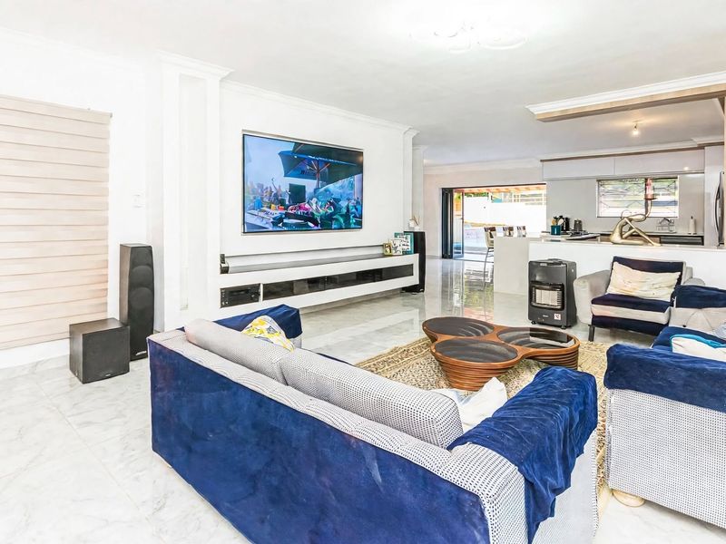 Spacious open-plan living area featuring polished marble-look flooring, a modern built-in media console, and a seamless transition to the kitchen and outdoor patio.