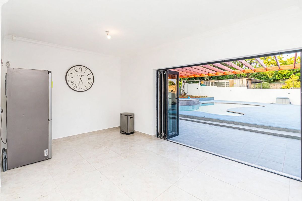 Bright and spacious living area featuring large bi-fold doors that open directly onto a paved patio and swimming pool area.