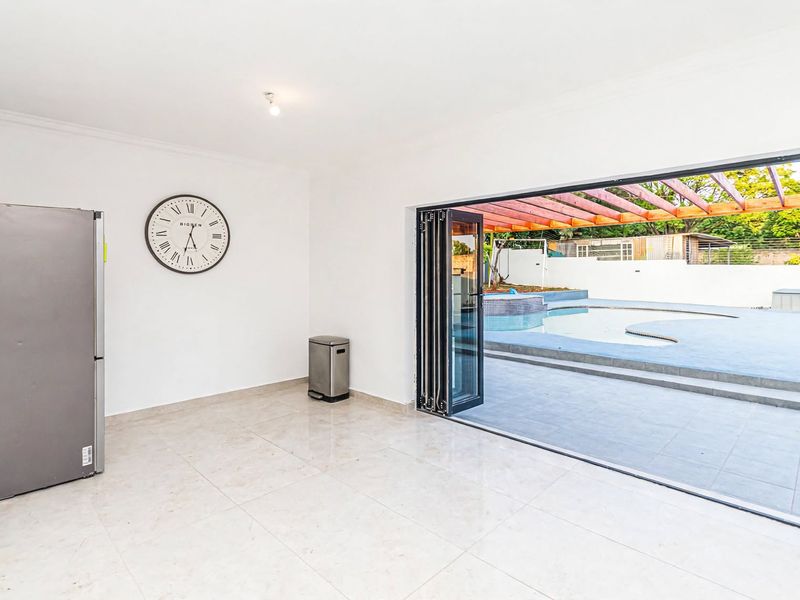 Bright and spacious living area featuring large bi-fold doors that open directly onto a paved patio and swimming pool area.