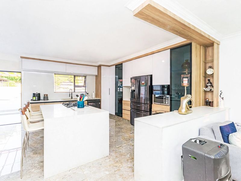 Modern open-plan kitchen featuring a large central island, sleek white cabinetry, stone countertops, and integrated appliances, seamlessly flowing into the living area.