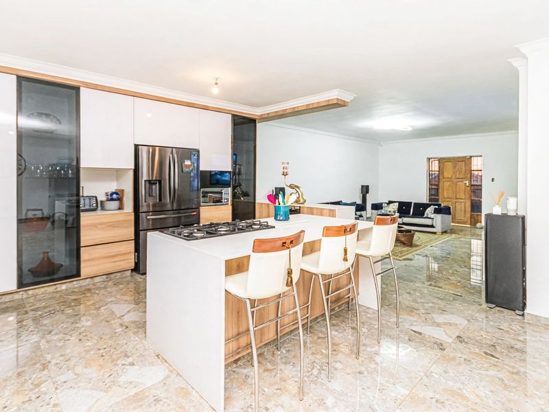 Modern open-plan kitchen featuring a central island with a gas cooktop, sleek cabinetry, and polished marble-look tile flooring flowing into the living area.