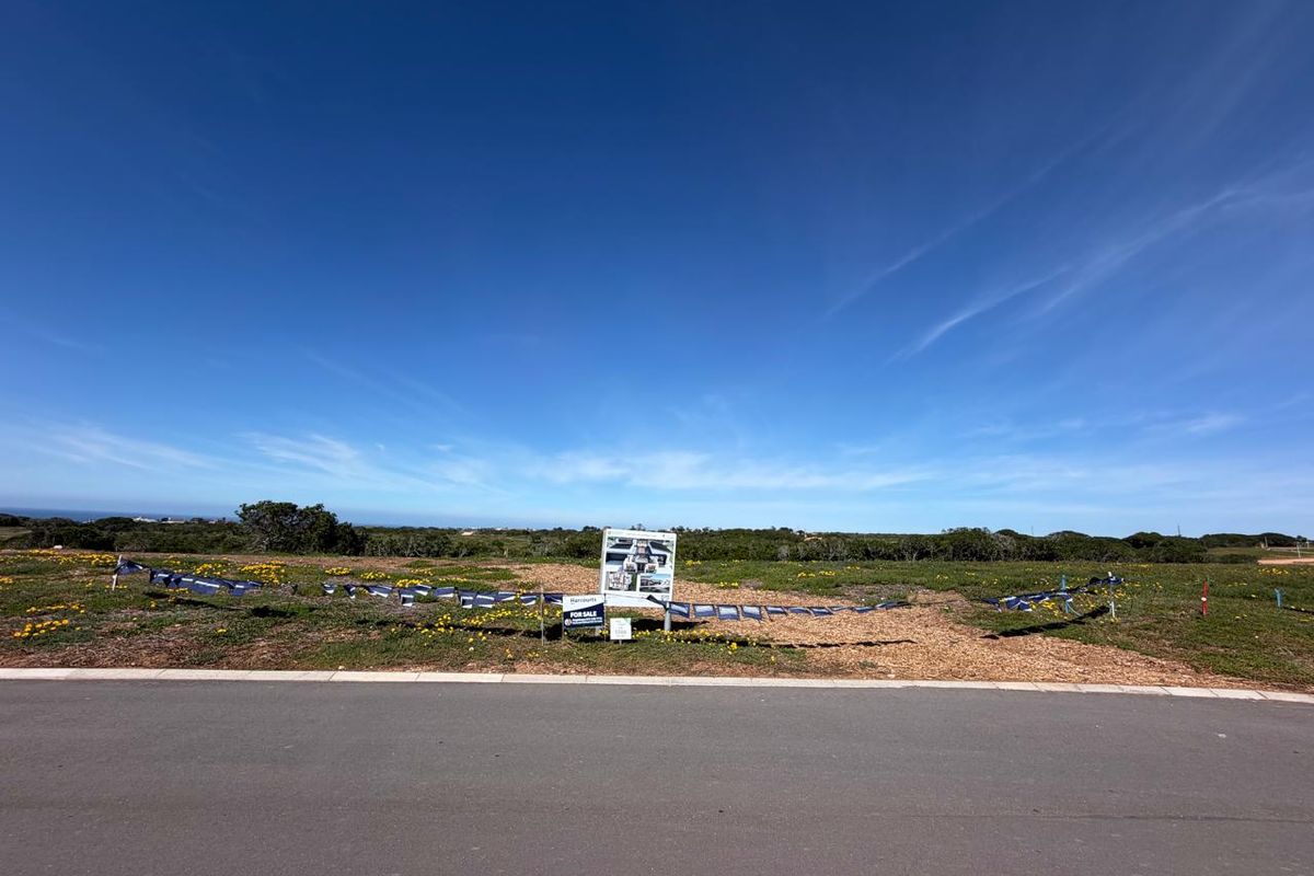 A vacant residential plot of land featuring a paved road frontage and existing real estate signage, set in a clear, open landscape.