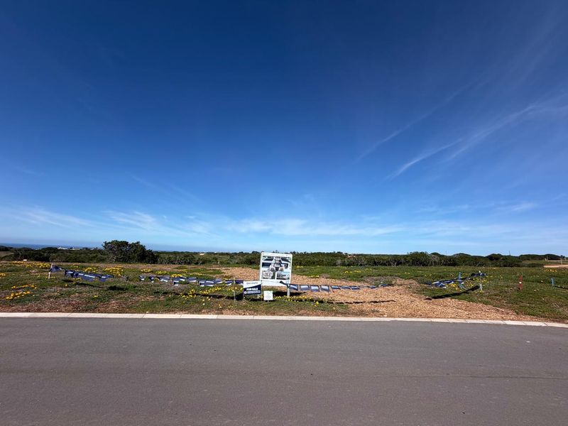 A vacant residential plot of land featuring a paved road frontage and existing real estate signage, set in a clear, open landscape.