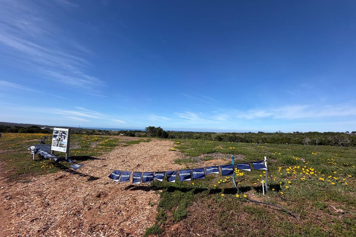 A wide-angle view of a vacant residential plot featuring natural vegetation, clear blue skies, and a real estate sign indicating the property for sale.