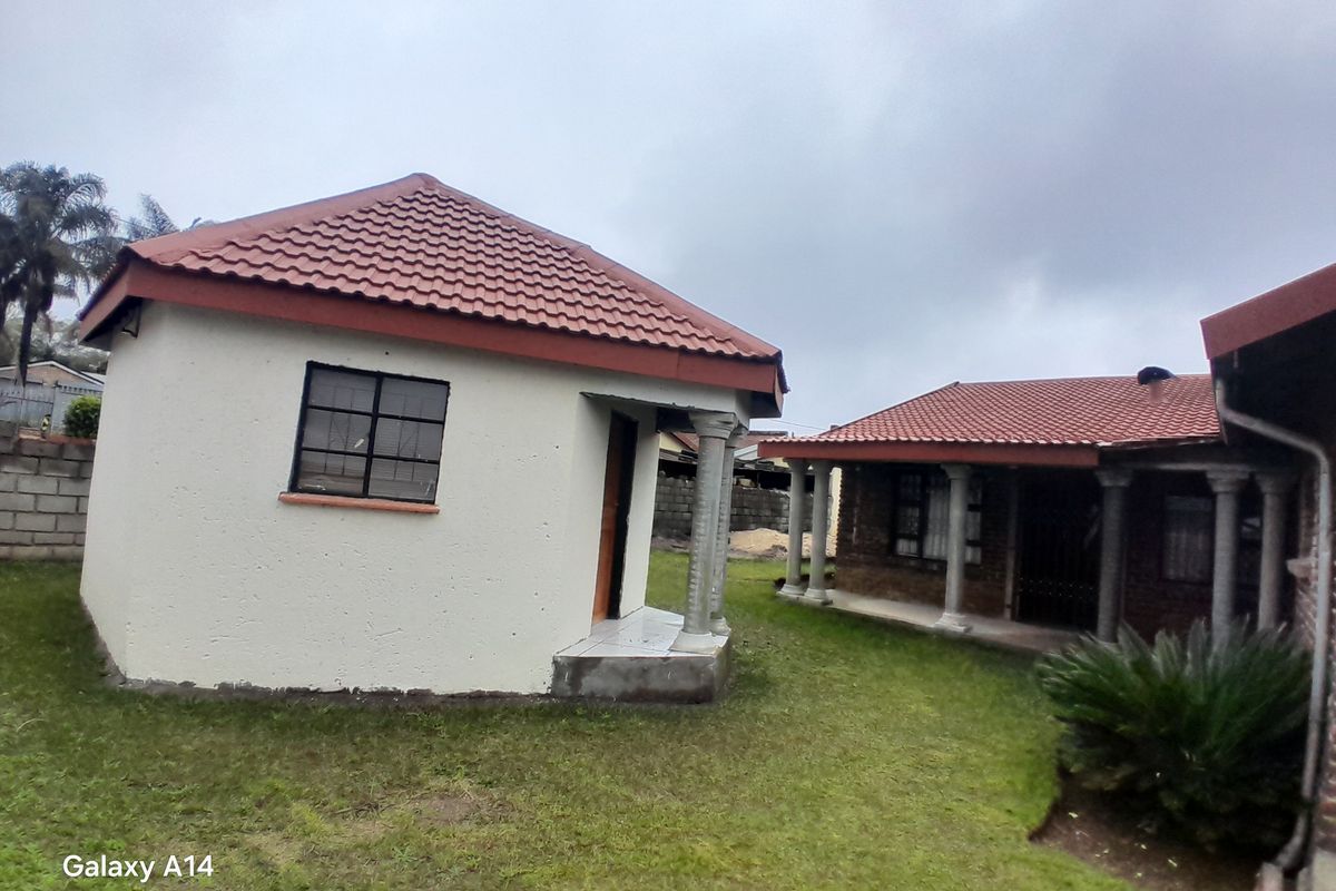 Rear view of the property featuring a detached structure with a tiled roof, concrete columns, and a surrounding lawn area.