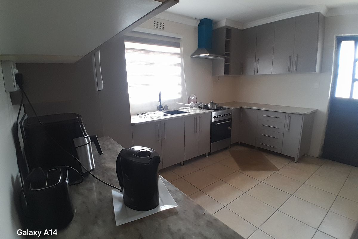 Functional kitchen featuring grey built-in cabinetry, laminate countertops, tiled flooring, and a stainless steel extractor fan with a freestanding oven.