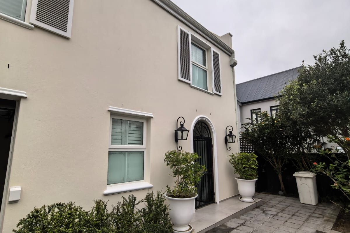 A well-maintained rear exterior view featuring a paved patio area, arched entrance, and classic window shutters.