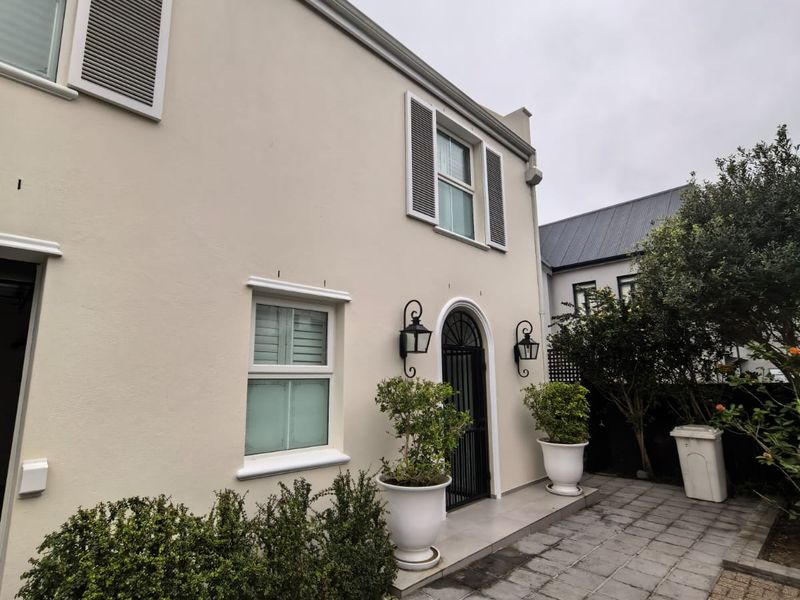 A well-maintained rear exterior view featuring a paved patio area, arched entrance, and classic window shutters.