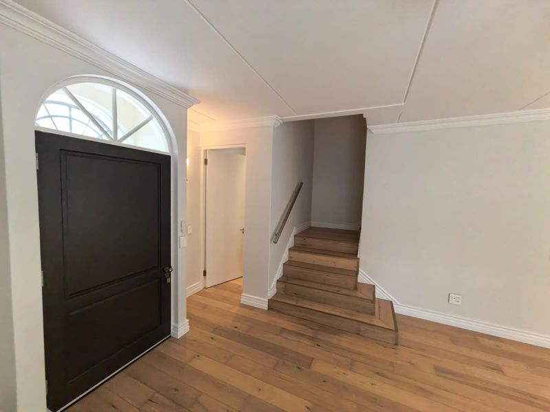 A bright and welcoming entrance hall featuring timber flooring, crown molding, and a staircase with a modern handrail.