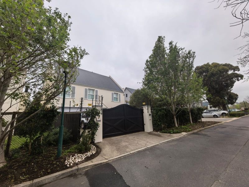 Front exterior view of a two-story house featuring a paved driveway, secure solid gate, and electric fencing.