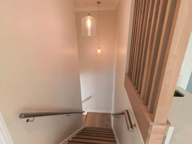 A modern staircase featuring timber treads, a stylish timber slat balustrade, stainless steel handrails, and contemporary pendant lighting.