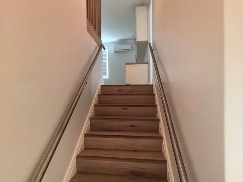 A bright, modern staircase featuring timber treads and sleek metal handrails, leading to an upper landing with integrated air conditioning.