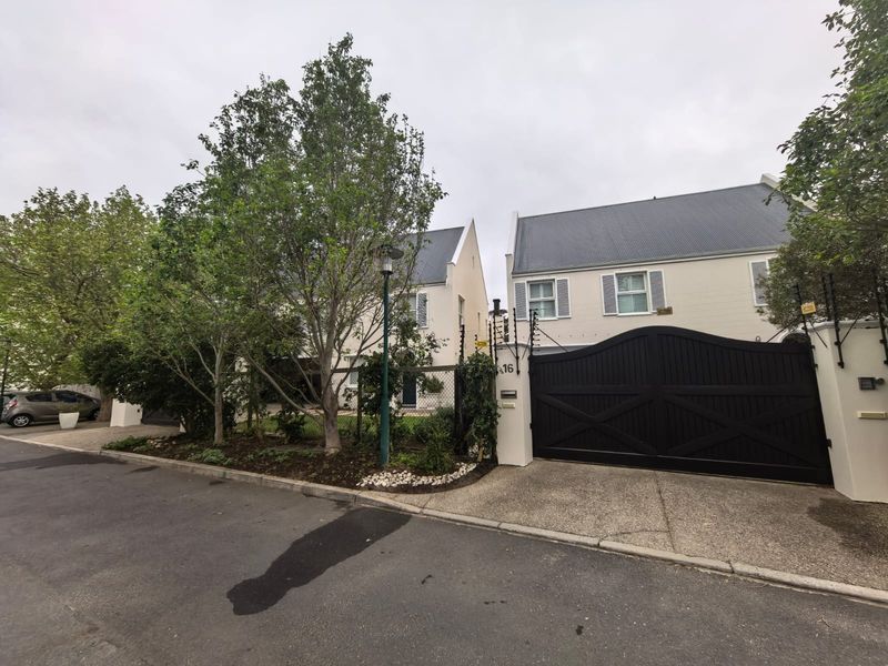 Front elevation of a residential property featuring a secure gated entrance, paved driveway, and established garden landscaping.