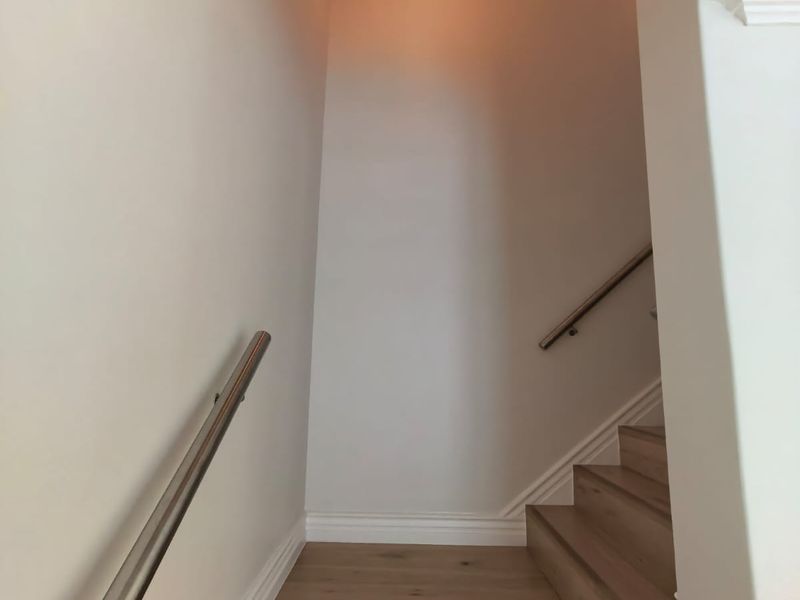 A clean, modern staircase featuring timber treads, stainless steel handrails, and crisp white walls with elegant skirting boards.