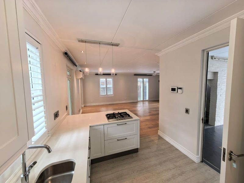 Modern open-plan kitchen and living area featuring shaker-style cabinetry, quartz countertops, gas hob, timber flooring, and plantation shutters.
