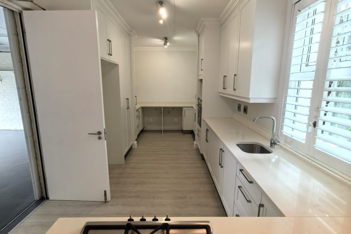 Modern kitchen featuring white shaker cabinetry, quartz countertops, a gas hob, and plantation shutters, offering a clean and functional workspace.