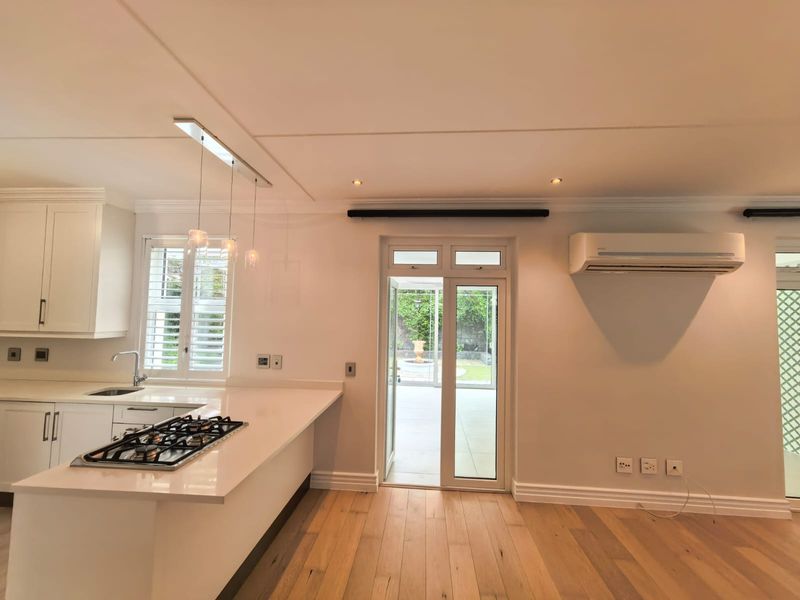 Modern open-plan kitchen featuring white cabinetry, quartz countertops, gas hob, and timber flooring, with direct access to the rear patio area.