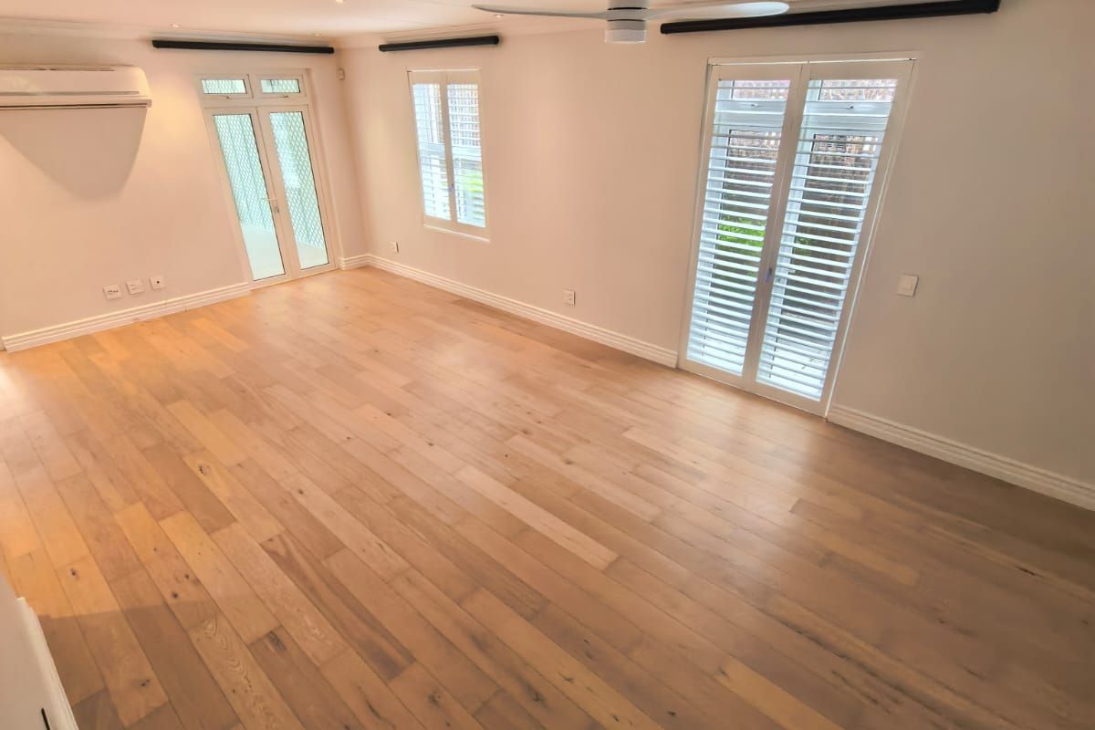Spacious living area featuring light timber flooring, plantation shutters, ceiling fan, and split-system air conditioning with direct access to the exterior.