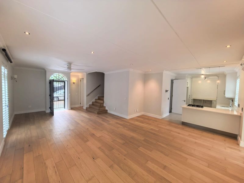 Spacious open-plan living area featuring light hardwood flooring, recessed lighting, a modern kitchen island with a built-in hob, and an elegant staircase.